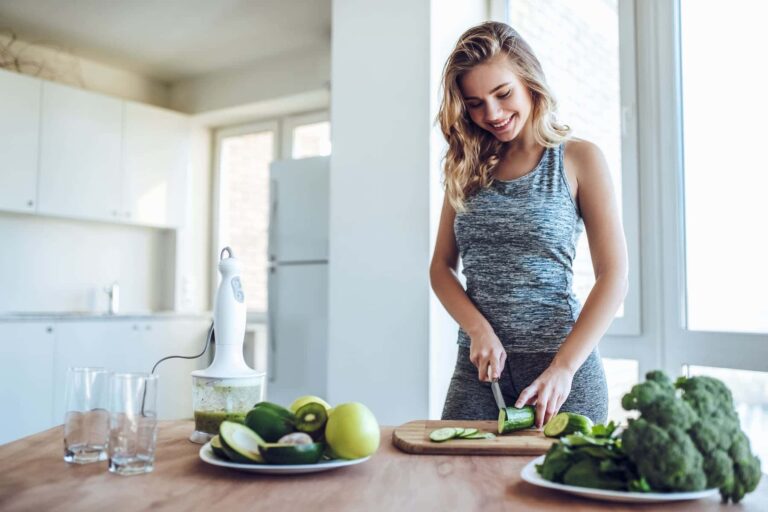 A woman cuts cucumbers in her kitchen after a workout, following her daily routine for a healthy lifestyle.
