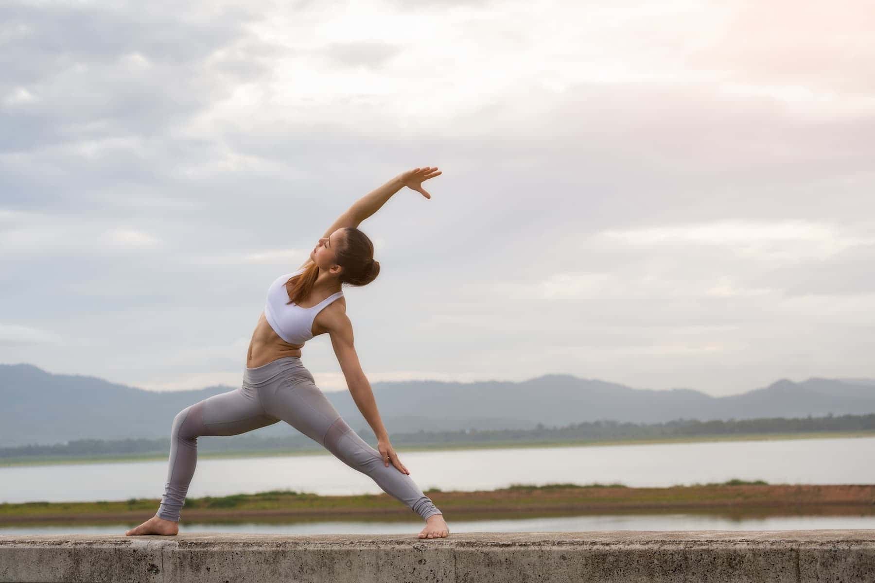 A woman practices calming yoga outdoors in nature, showcasing one of the many different types of yoga.