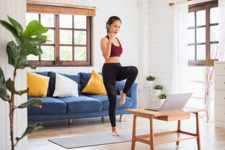 A woman enjoys her home exercise routine in the living room, smiling as she follows an exercise video on her laptop.