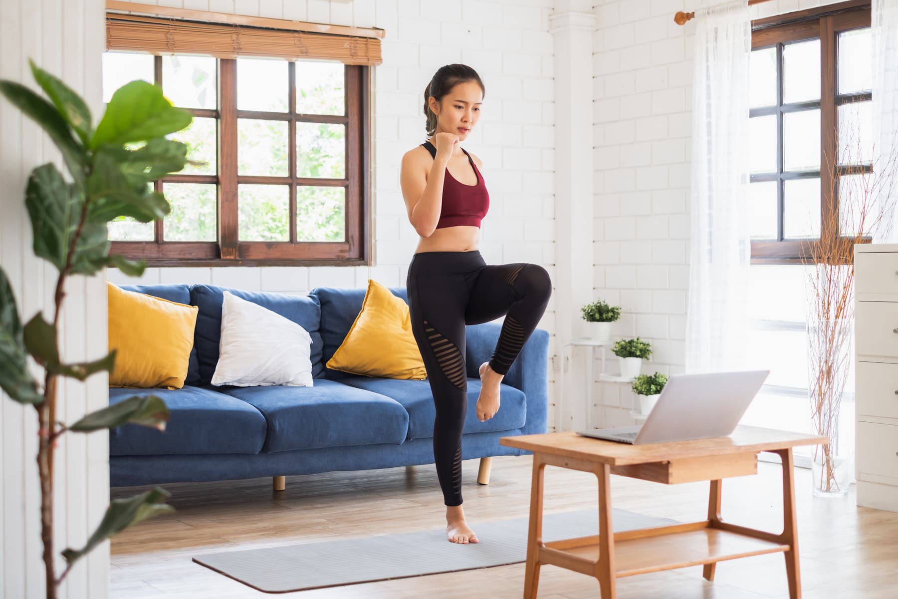 A woman enjoys her home exercise routine in the living room, smiling as she follows an exercise video on her laptop.