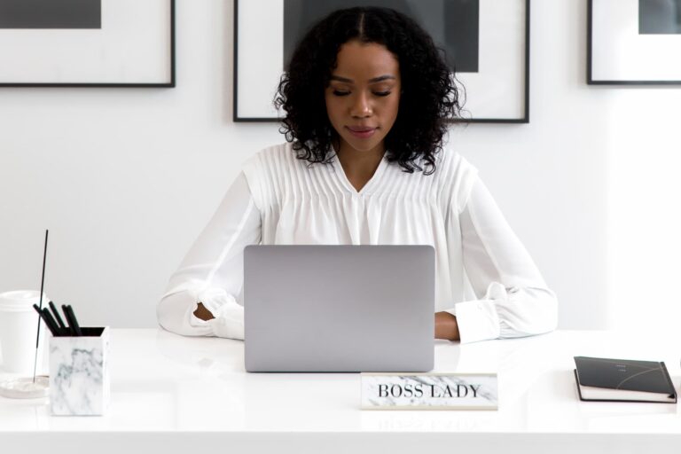 Woman working on a laptop with a ‘Boss Lady’ nameplate, representing a blogging business using legal templates.