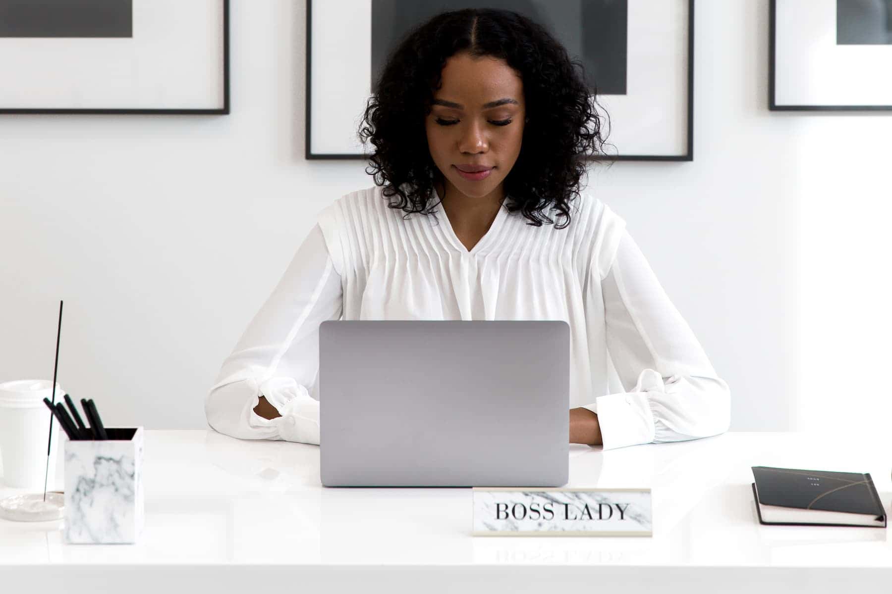 Woman working on a laptop with a ‘Boss Lady’ nameplate, representing a blogging business using legal templates.