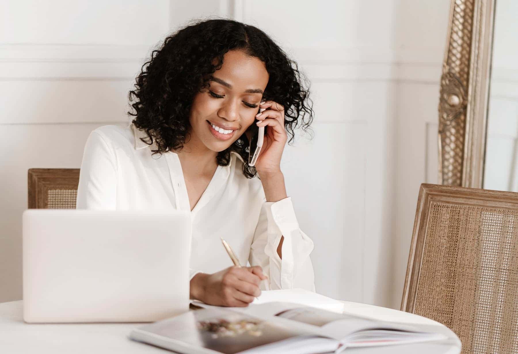 Woman working on a laptop while taking notes and talking on the phone, representing managing a website with premium web hosting.