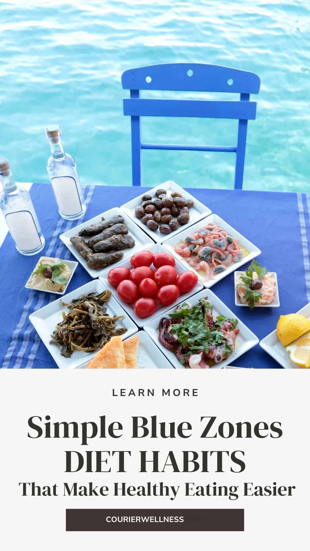 Table set with appetizers, including olives, dolmades, shrimp, octopus, tomatoes, lemons, and bread, overlooking blue water.