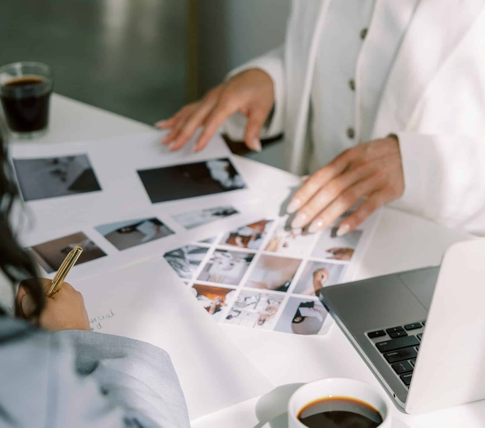 Two people collaborate at a table, reviewing a printed mood board while taking notes beside an open laptop.